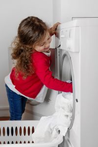 Blond little girl filling tumble dryer with laundry