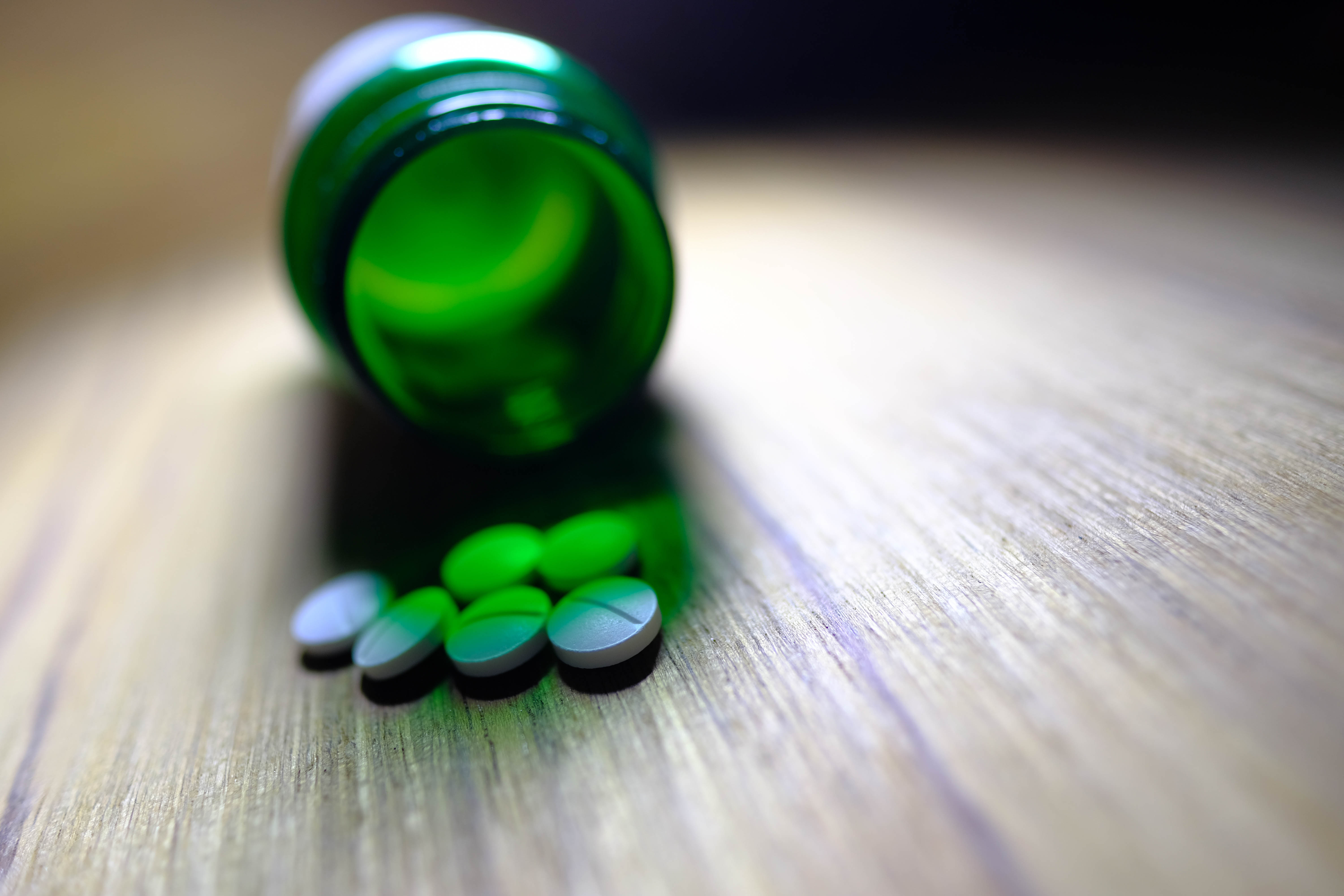 While pills spilling out of green pill bottle