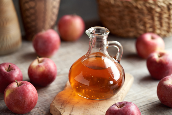 A jug of apple cider vinegar with fresh apples