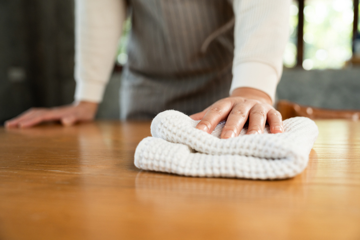 Housewife with apron ready to clean home. Young woman is happy to clean home. Maid cleaning service. Spraying antibacterial sanitizing spray wipe with towel